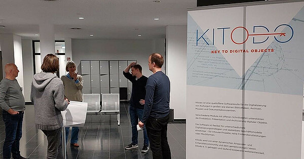 Standup-Meeting mit Poster im Vordergrund
